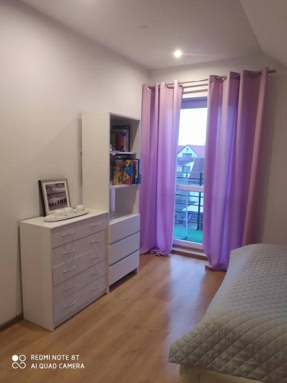 ein Schlafzimmer mit lila Vorhängen, einer Kommode und einem Fenster in der Unterkunft Apartament u Małgosi in Kołczewo