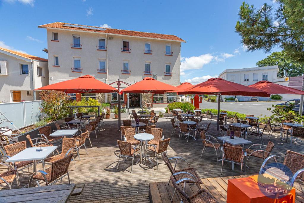 eine Terrasse mit Tischen, Stühlen und roten Sonnenschirmen in der Unterkunft Hôtel Les Pins in Saint-Trojan-les-Bains