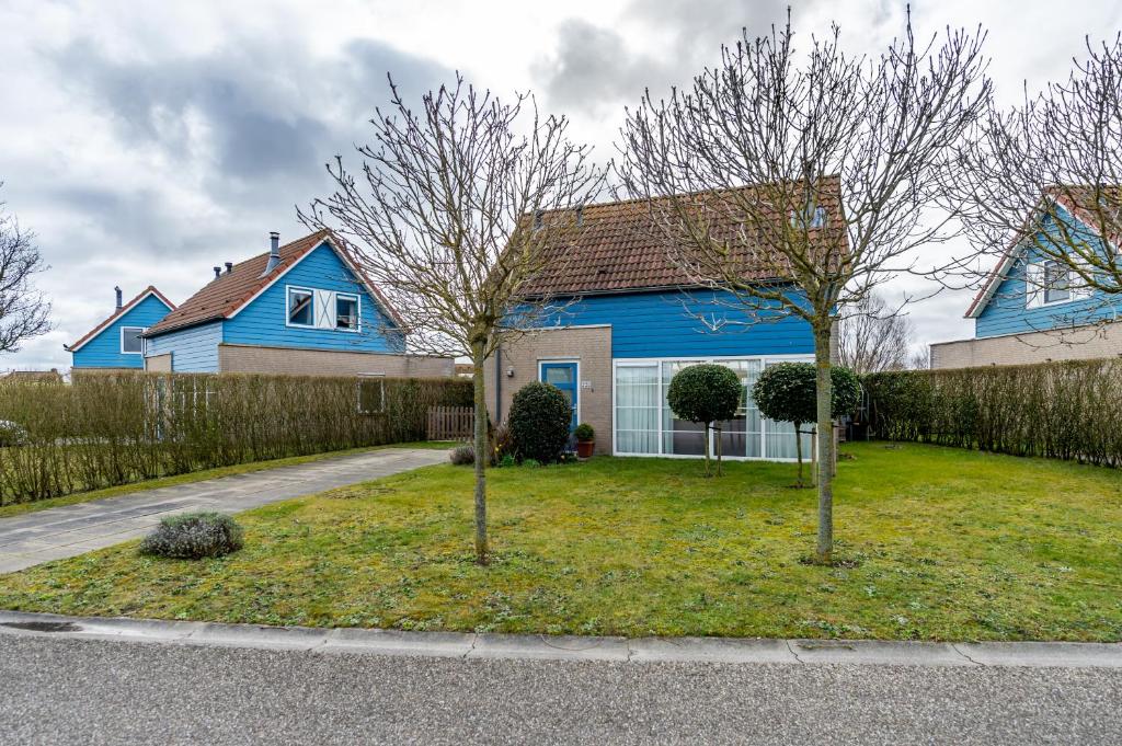 a blue house with two trees in the yard at Antibes 232 - Kustpark Village Scaldia in Hoofdplaat