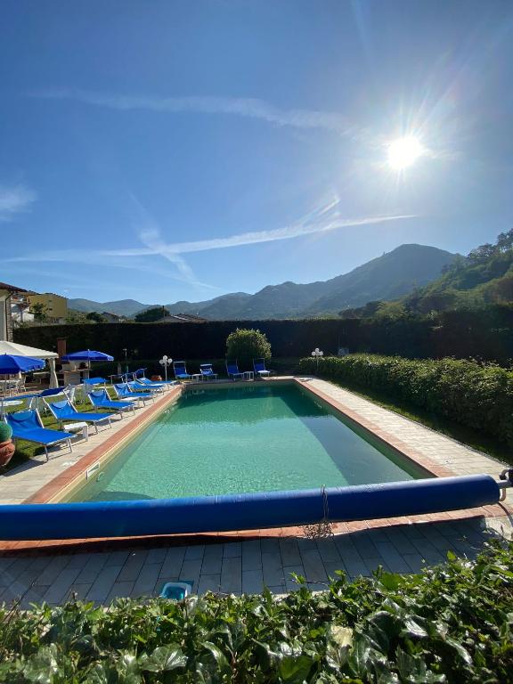 une grande piscine avec des chaises bleues et des montagnes en arrière-plan dans l'établissement Villa con piscina Privata tra Versilia e Cinque Terre, à Luni