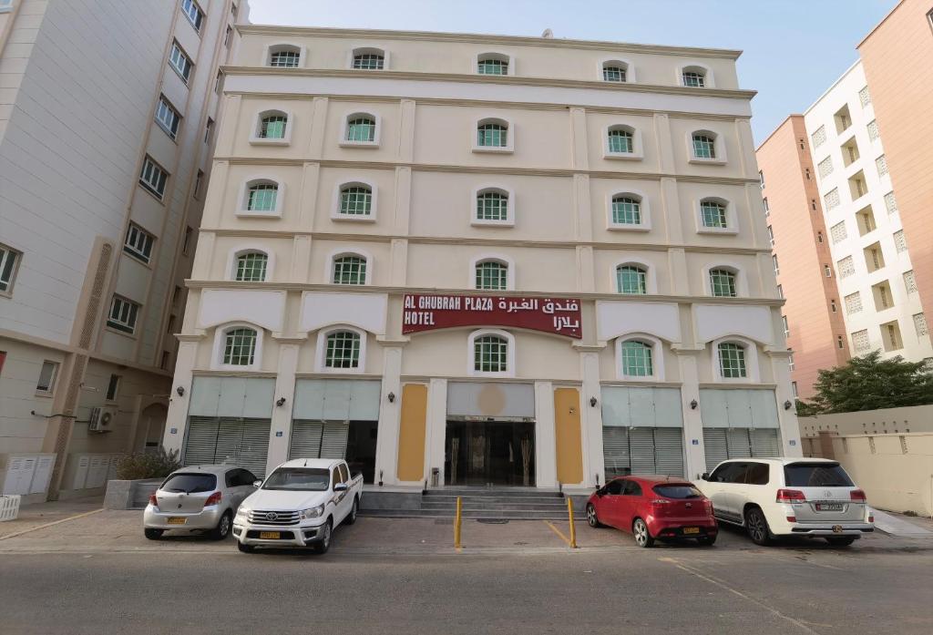 a large building with cars parked in a parking lot at Al Ghubrah Plaza Hotel in Muscat