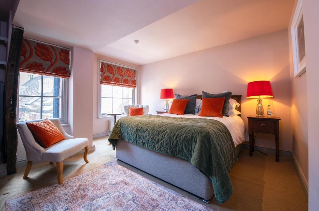 a bedroom with a bed and a chair and two windows at RHUBARB at Drapers Hall in Shrewsbury