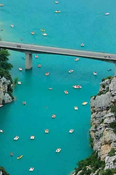 un groupe de bateaux dans l'eau sous un pont dans l'établissement Camping prés des Gorges du Verdon et Du Lac De Ste Croix 04500 Tout Equipé Confort Calme Lavande, à Sainte-Croix-de-Verdon