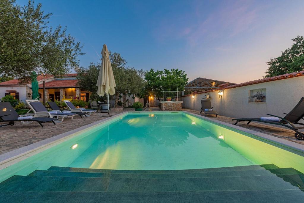 a swimming pool in a backyard with chairs and a umbrella at Villa Štrkalj ZadarVillas in Murvica