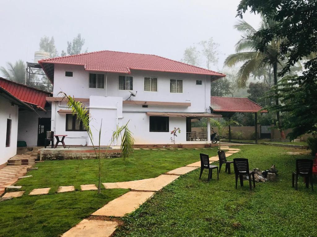 a white house with chairs in the yard at Greenhouse Homestay in Siddapur