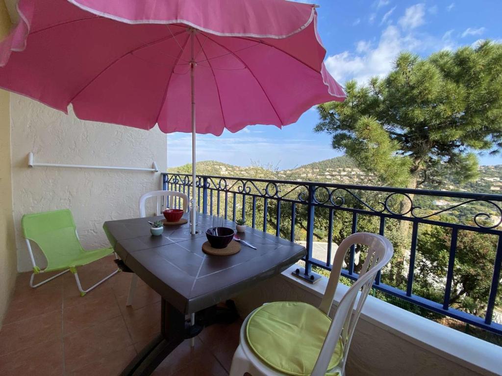 einen Tisch und Stühle auf einem Balkon mit einem rosa Regenschirm in der Unterkunft Appartement Les Issambres, 1 pièce, 4 personnes - FR-1-226-84 in Les Issambres