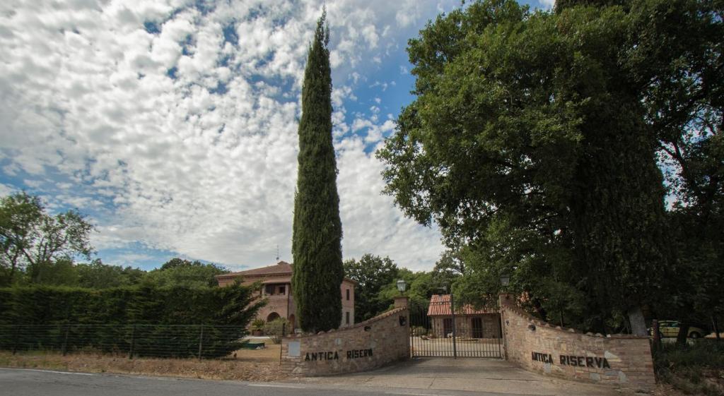 a house with a tall tree in front of a fence at Antica Riserva in Castiglione del Lago