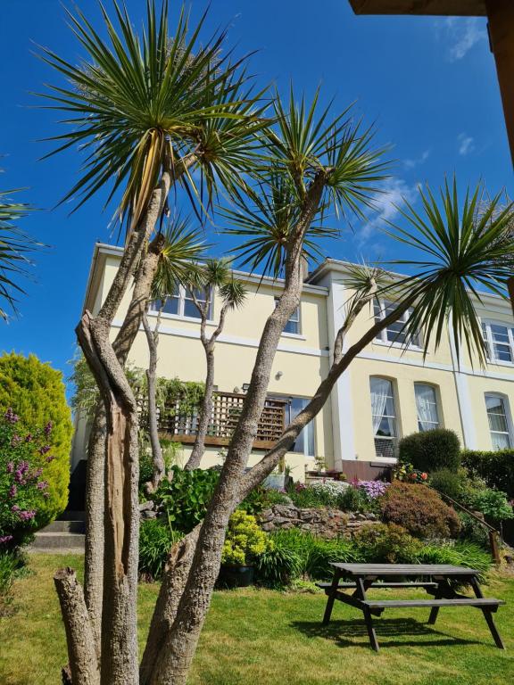 a picnic table in front of a house with palm trees at Meadowside Holiday Apartments in Torquay