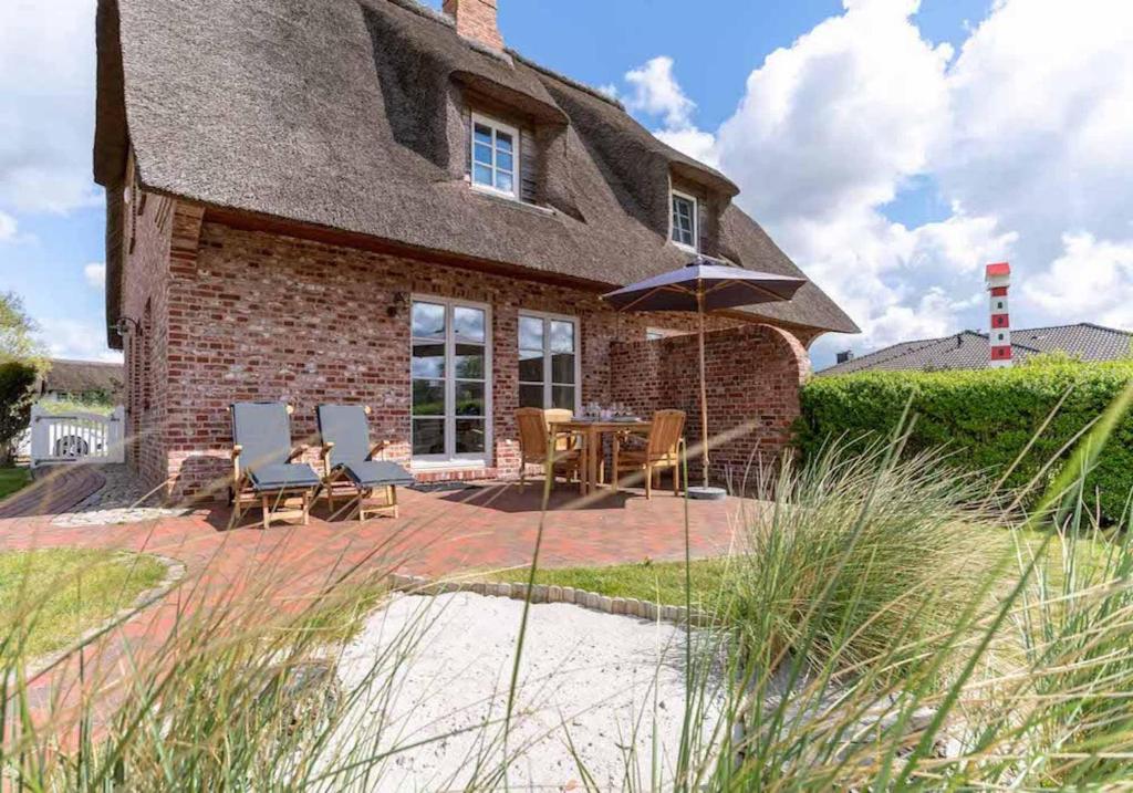 a house with a patio with chairs and an umbrella at Reetdachhaus Seaside Reetdachhaus Seaside in Süderhöft