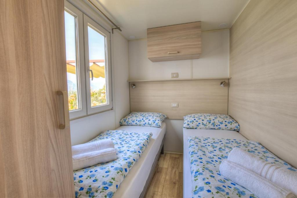 two beds in a small room with two windows at Agricampeggio Relax Maxicaravan in Castelletto di Brenzone