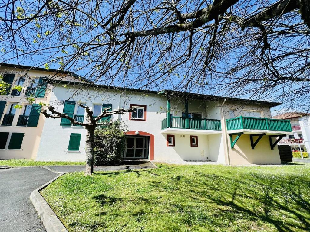 une maison blanche avec des fenêtres vertes et une cour dans l'établissement T2 calme avec balcon, parking et internet, Cambo-les-Bains - FR-1-495-46, à Cambo-les-Bains