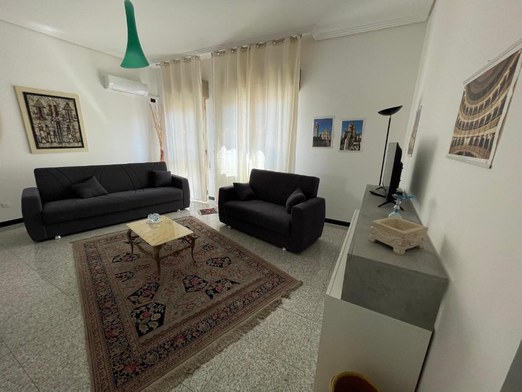 Sala de estar con 2 sofás negros y TV en Vincenti's House Comiso en Comiso