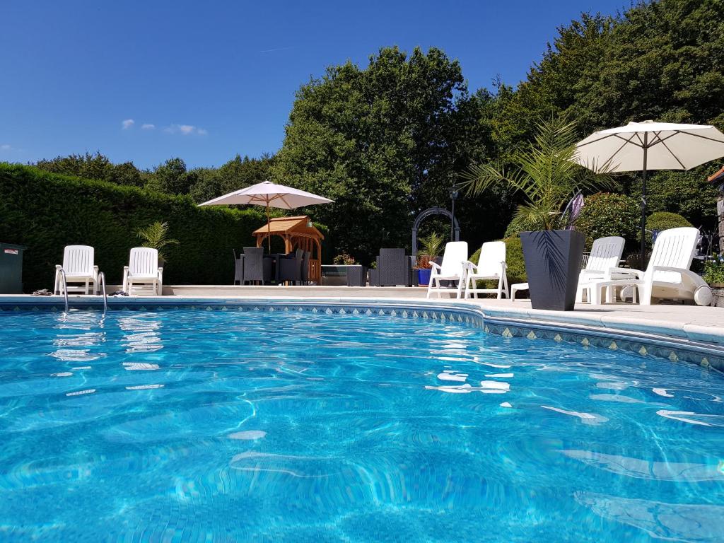 a swimming pool with white chairs and umbrellas at Maroux Vian Country Cottage in Callac