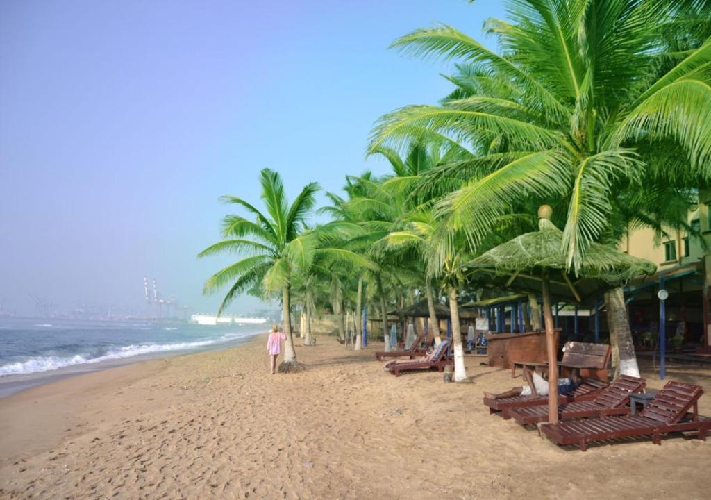 a beach with palm trees and a person walking on the beach at COCOBEACH-HOTEL in Lomé