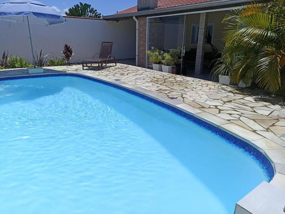 a large blue swimming pool with a patio and a house at Casa com piscina aquecida em Itapoá in Itapoa