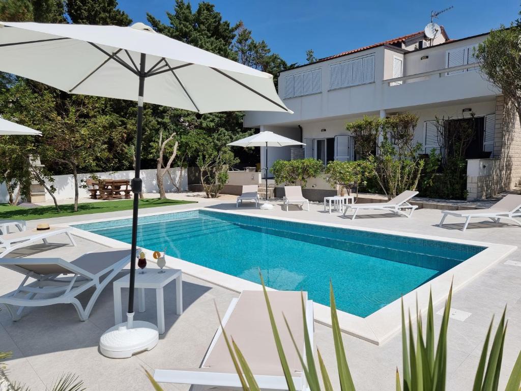 - une piscine avec des chaises et un parasol à côté d'une maison dans l'établissement Villa FLAMINGO Deluxe Novalja, à Novalja