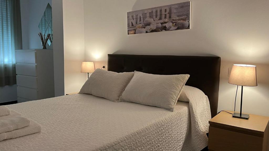 um quarto com uma cama com lençóis brancos e 2 candeeiros em Apartamento Puente Romano em Córdoba