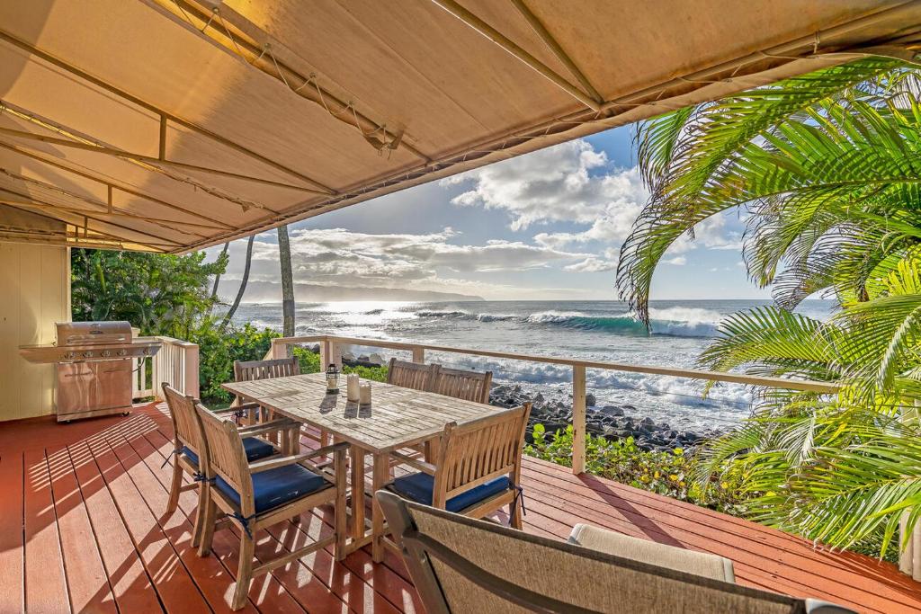 a table and chairs on a deck with a view of the ocean at Waimea Bay Shoreline House in Haleiwa