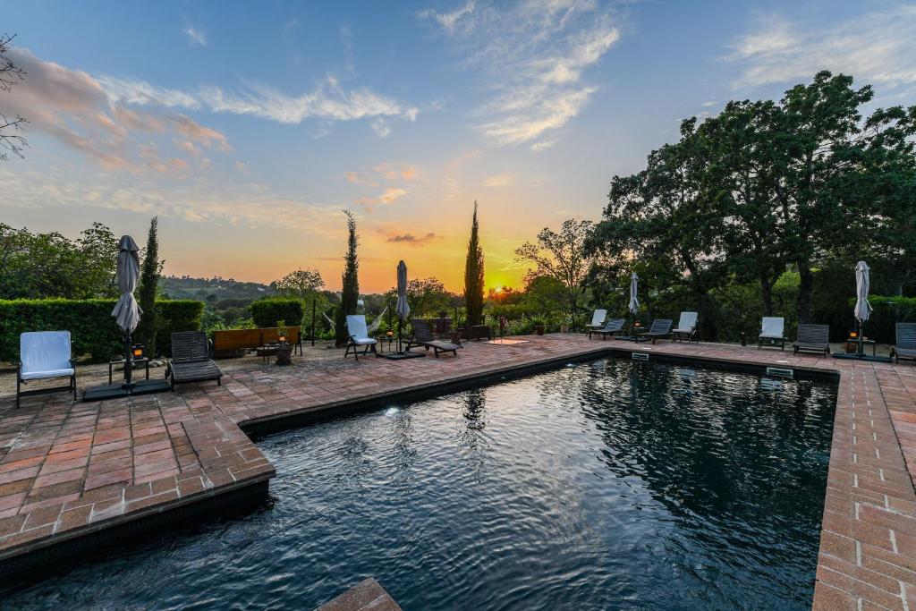 a swimming pool with chairs and a sunset in the background at Quinta da Dourada in Portalegre