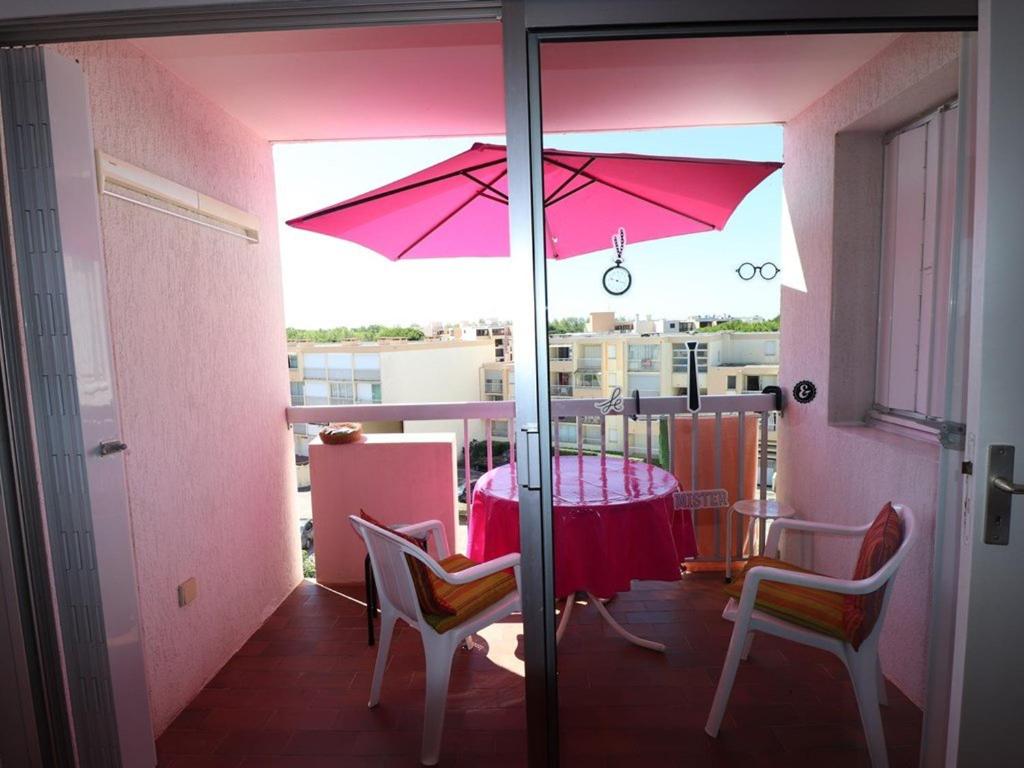 une table rouge et des chaises avec un parasol sur un balcon dans l'établissement 2 pièces Cabine, Terrasse Sud, proche mer & commerces, Le Grau-du-Roi - FR-1-307-163, au Grau-du-Roi