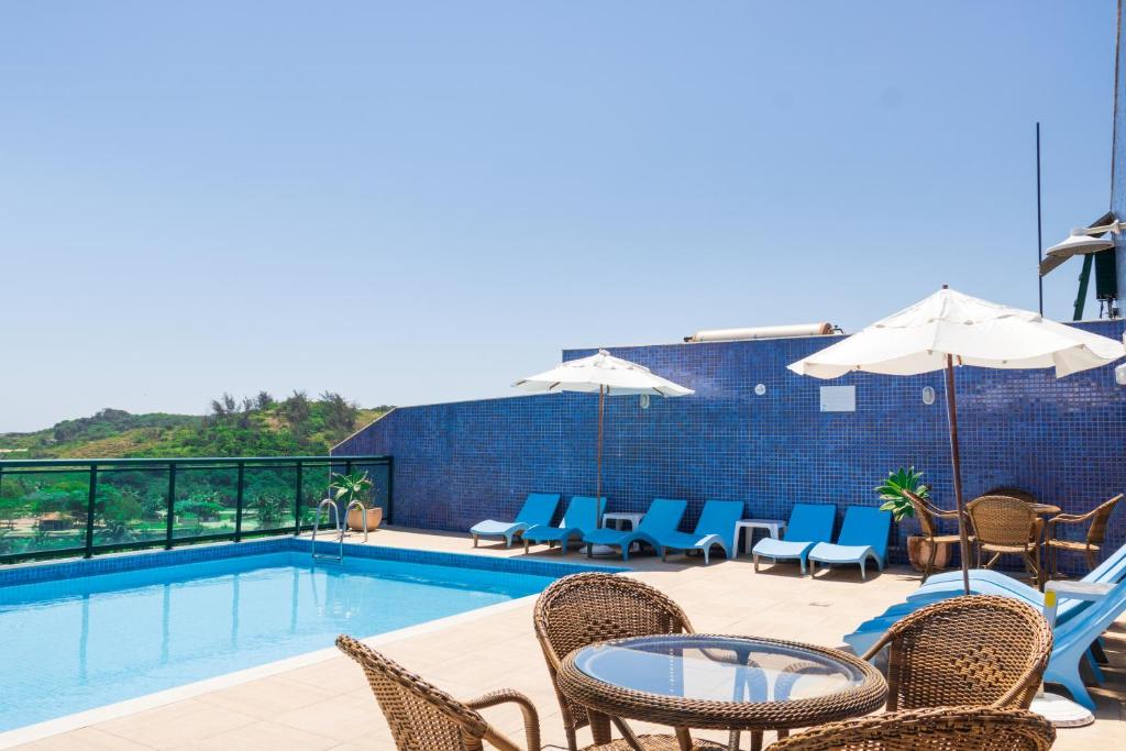 a swimming pool with chairs and a table and umbrella at Mediterrane Hotel by Castelo Itaipava in Arraial do Cabo