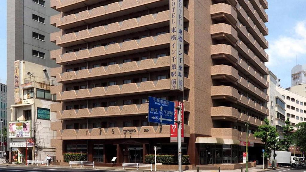 Toyoko Inn Chiba Ekimae في شيبا: مبنى طويل مع علامة زرقاء أمامه