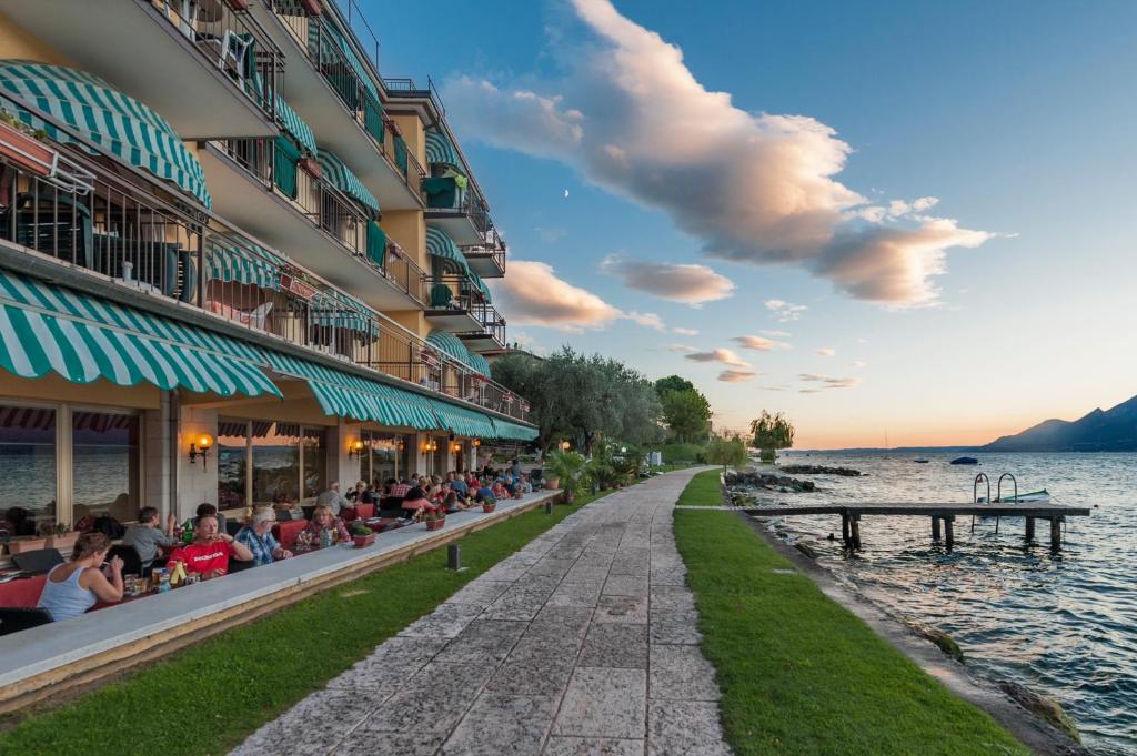 a group of people sitting outside of a building next to the water at Hotel Nettuno in Brenzone sul Garda