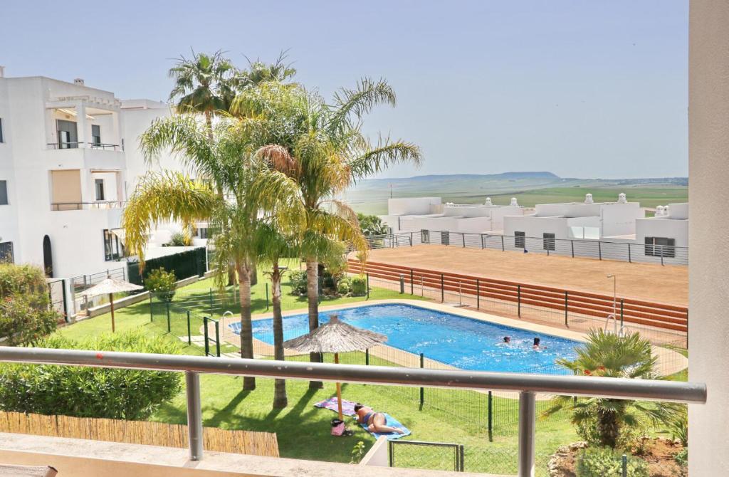 Blick auf einen Pool mit Palmen und Gebäuden in der Unterkunft Apartamento Río Salado in Conil de la Frontera
