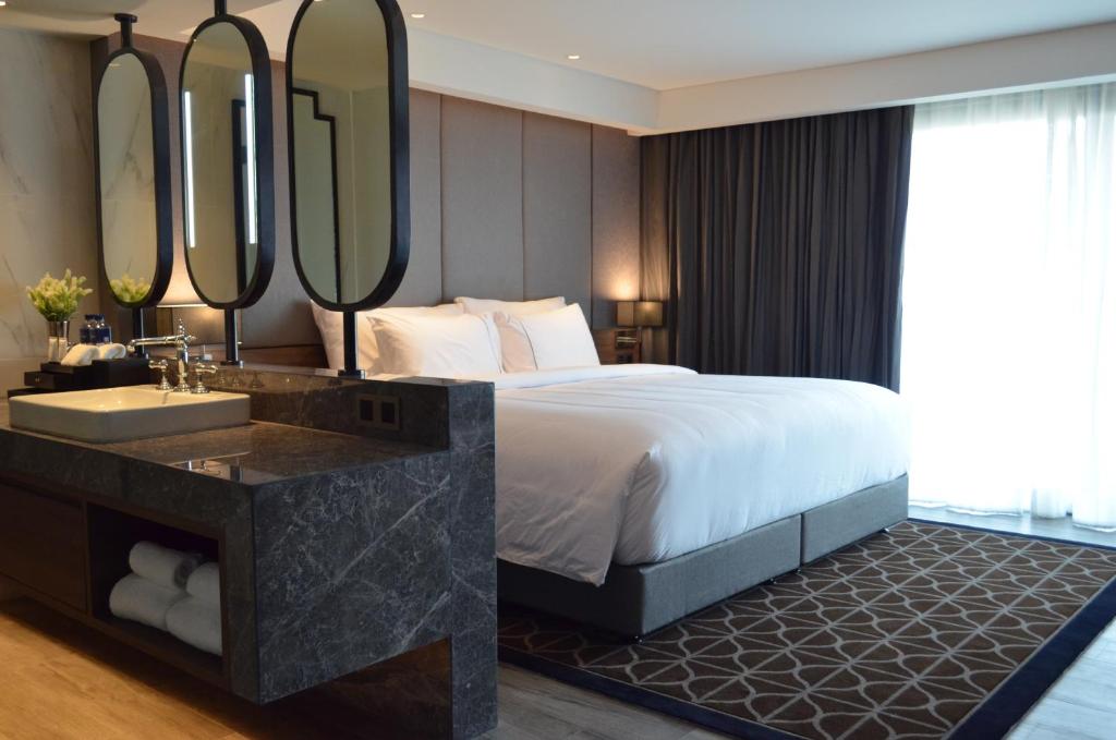 A bedroom with a large bed, marble open vanity, blackout curtains, and bright window light.