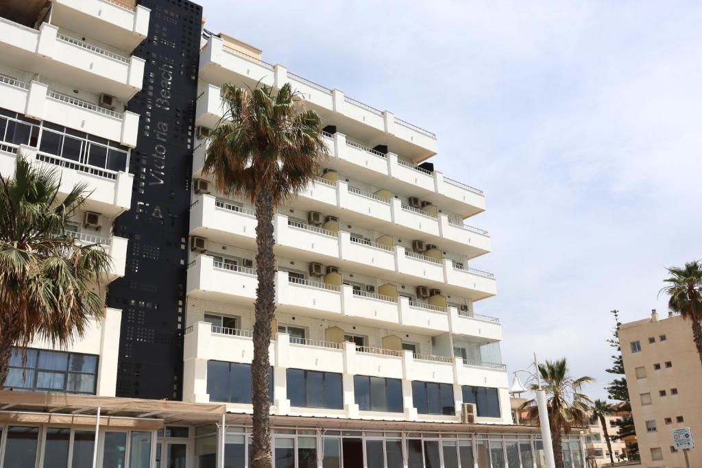 a tall white building with palm trees in front of it at FAY Victoria Beach in Rincón de la Victoria
