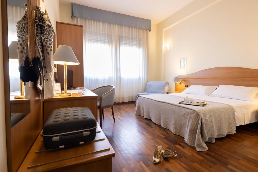 une chambre d'hôtel avec un lit et un bureau avec une valise dans l'établissement Hotel Il Duca d'Este, à Ferrare