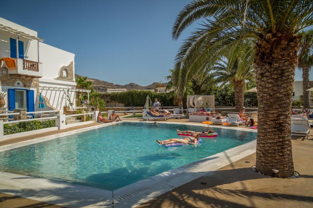 a group of people laying in a swimming pool with a palm tree at Hotel Aegeon in Mylopotas