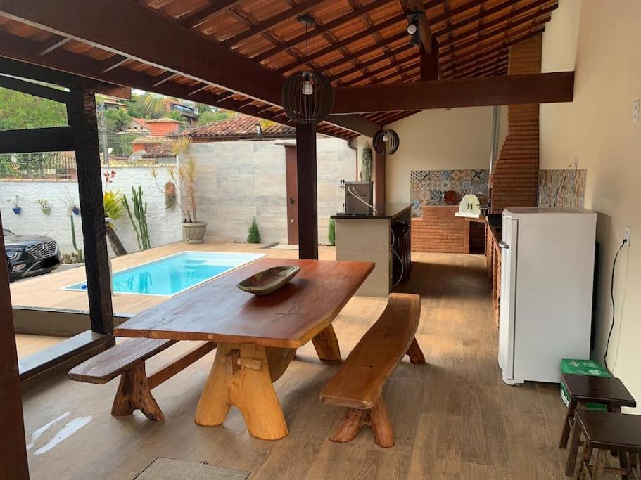 einen Holztisch und eine Bank in einer Küche mit einem Pool in der Unterkunft Búzios Geribá 2 minutos a pé da praia in Búzios