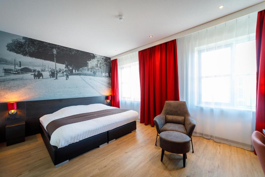 a bedroom with a bed and a chair and red curtains at Bastion Hotel Arnhem in Arnhem