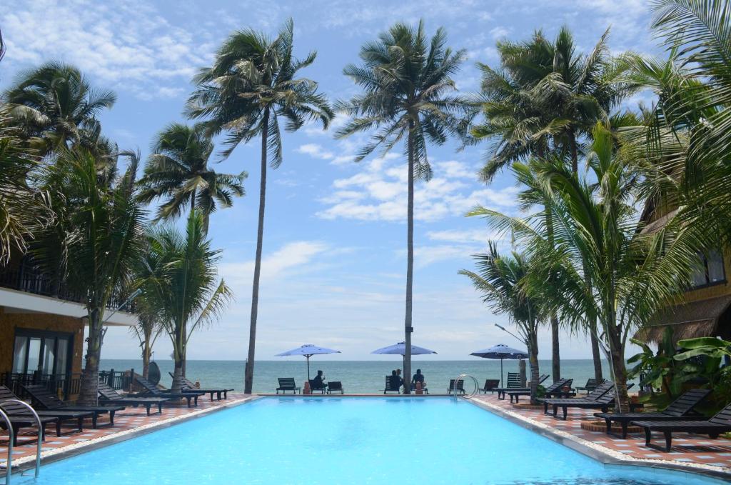 una piscina con palmeras y el océano en el fondo en Rang Garden Beach Side en Mui Ne