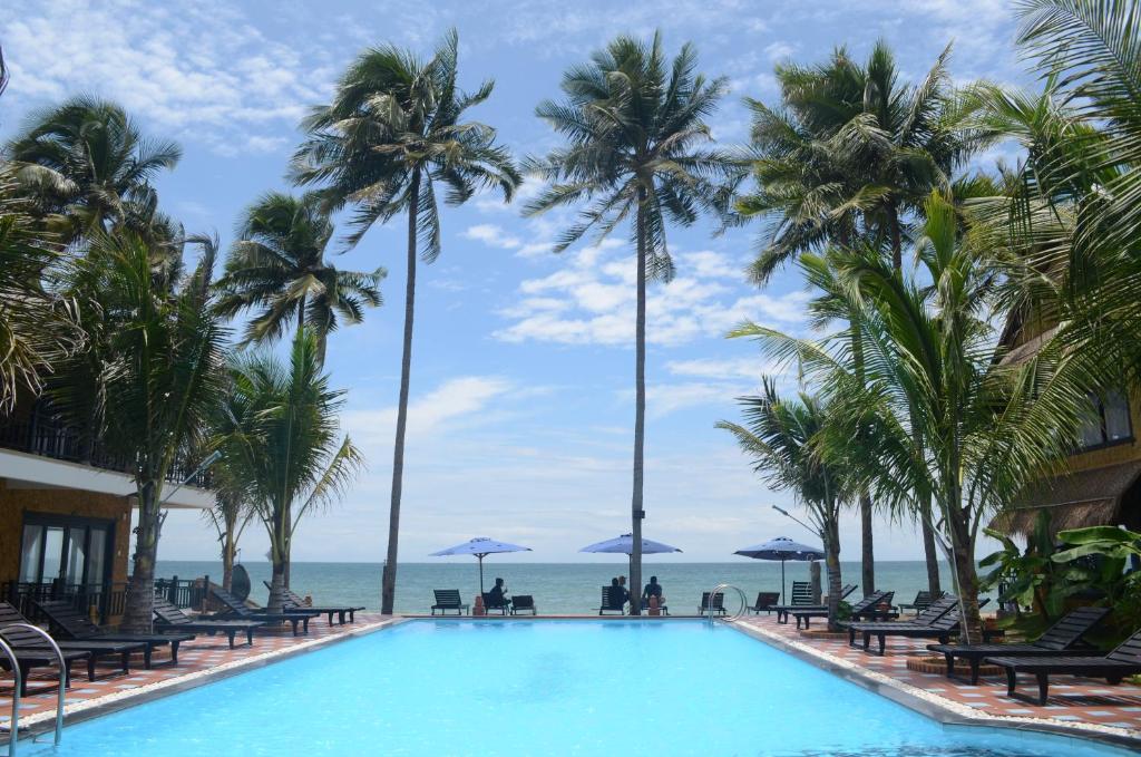 einen Pool mit Palmen und dem Meer im Hintergrund in der Unterkunft Rang Garden Beach Side in Mui Ne