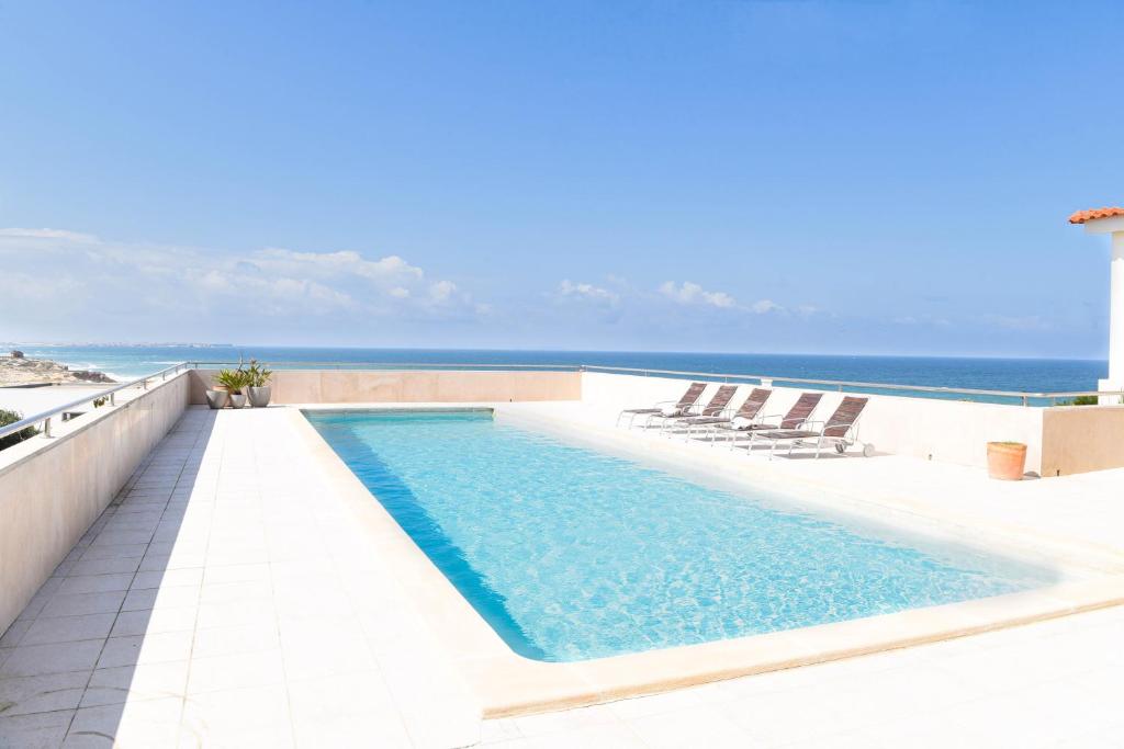 - une piscine avec des chaises et l'océan en arrière-plan dans l'établissement Vila Luxo da Praia, à Casal da Lagoa Seca