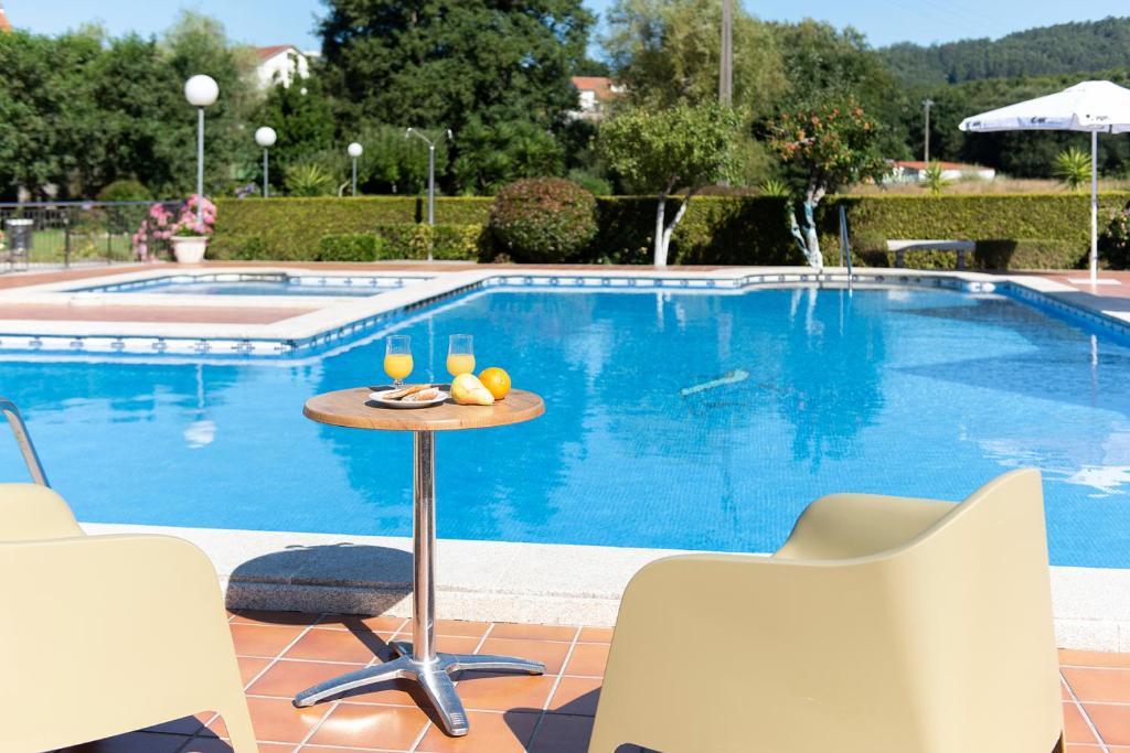 a table with two glasses of wine on it next to a swimming pool at Hotel Cabo Festiñanza in Sanxenxo