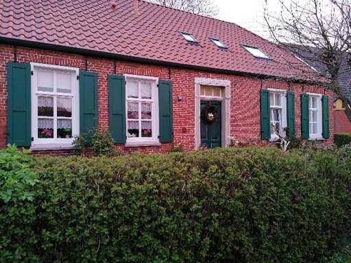 a red brick house with a red roof and green shutters at Alte Pastorei in Hinte