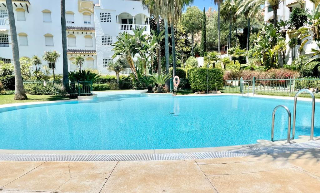 a large blue swimming pool with palm trees and a building at Hacienda de los Nagueles - EaW Homes in Marbella