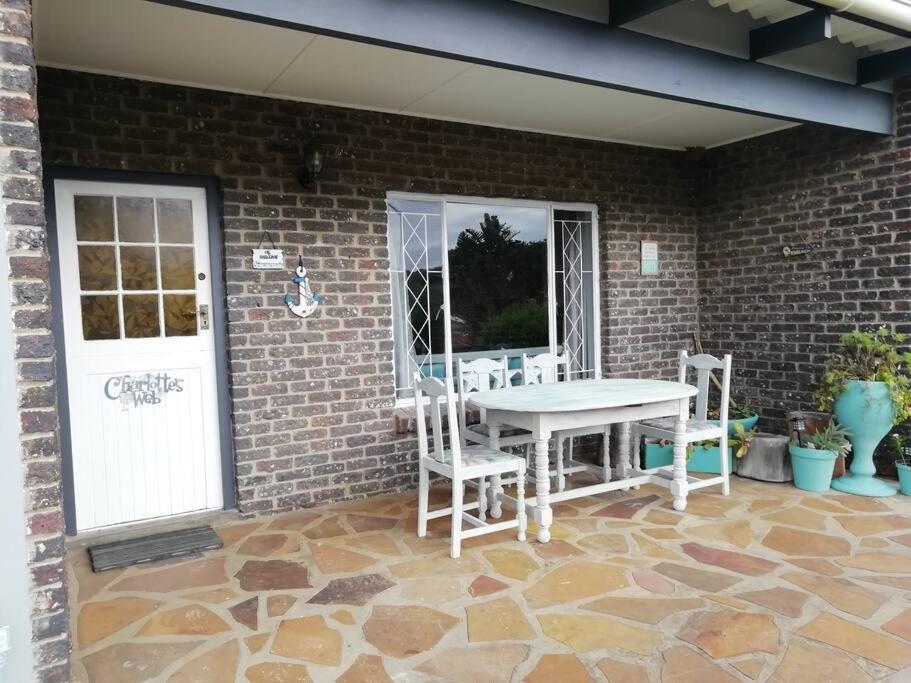 d'une terrasse avec une table et des chaises blanches sur un mur en briques. dans l'établissement Charlotte's Web - Beach Cottage - Queensberry Bay, à East London
