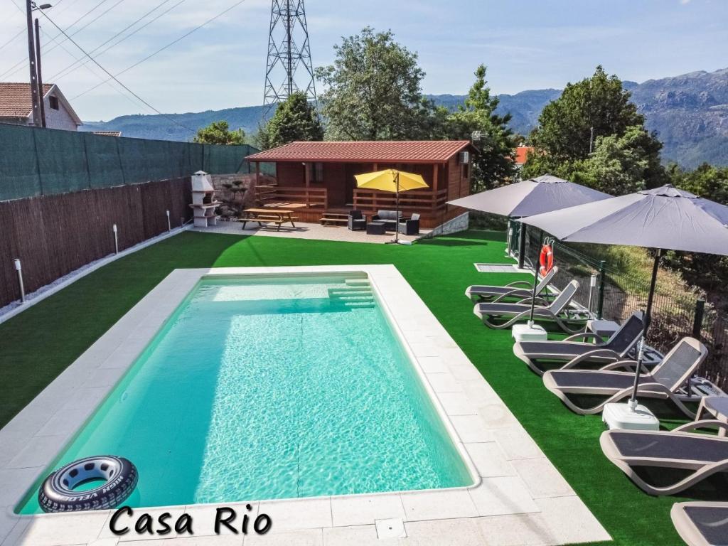 a swimming pool with chairs and umbrellas and a house at Encosta do Sonho in Vieira do Minho