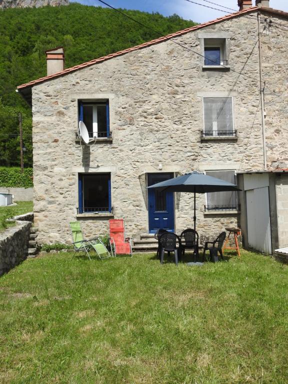 une maison en pierre avec des chaises et un parasol devant elle dans l'établissement Appartement T1 meublé haut vallespir le Tech, à Le Tech
