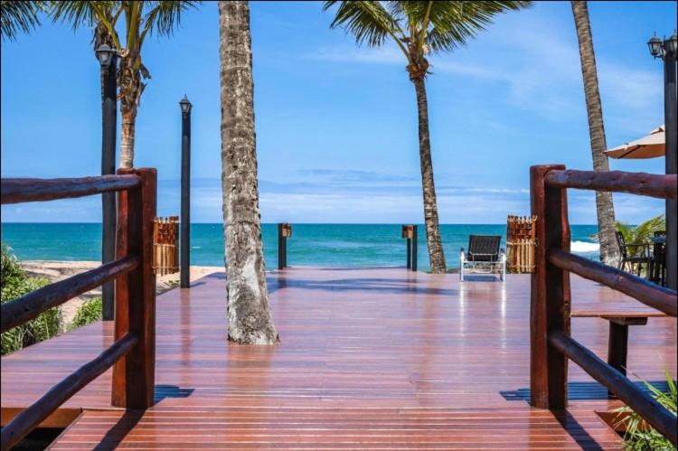 a wooden boardwalk with palm trees and the ocean at Vivant Eco Resort apartamento in Barra Grande
