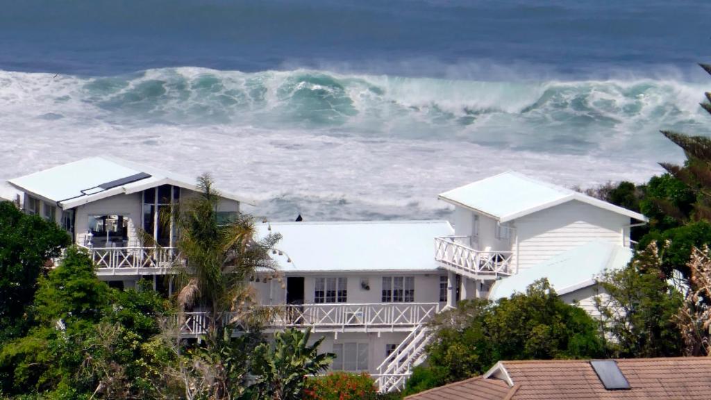 a large wave in front of a white house at Brenton Beach House in Brenton-on-Sea