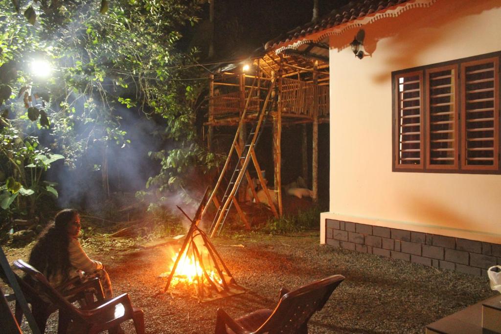 a woman sitting next to a fire in a yard at night at Wayanad Days in Mananthavady