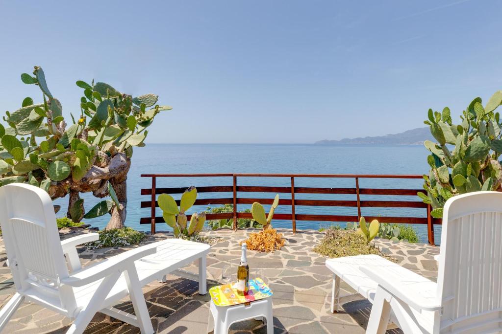 un patio con sillas blancas y una mesa con una botella de vino en La Terrazza sul Mare, en Magomadas