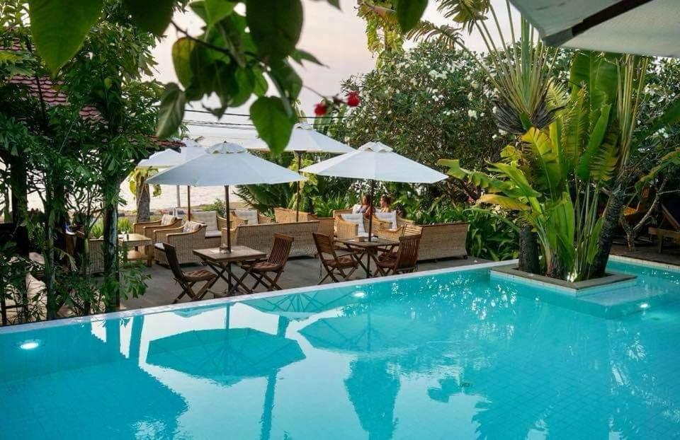 a pool with tables and chairs and umbrellas at Mealea Resort in Kep