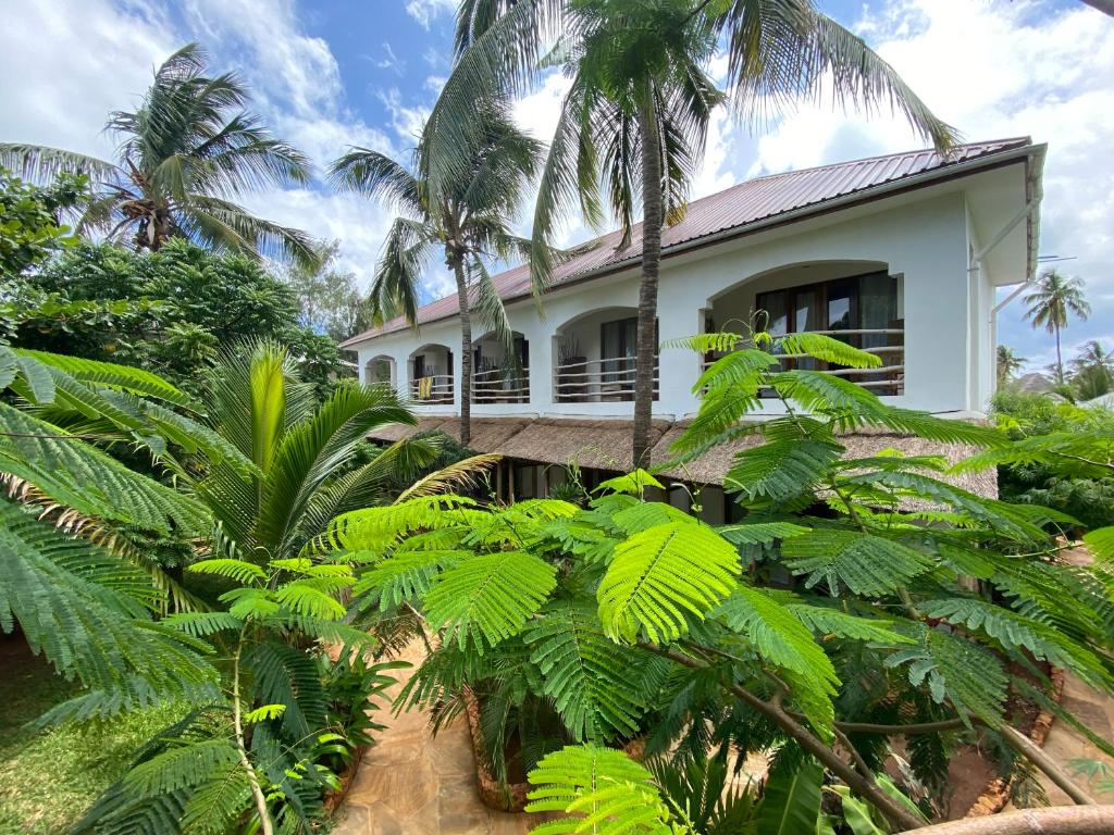 a white house with palm trees in front of it at Siri Beach Lodge in Nungwi