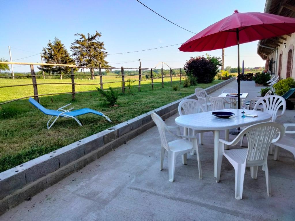 une table et des chaises blanches avec un parapluie rouge dans l'établissement La Grange à outeaux, à Montpont-en-Bresse